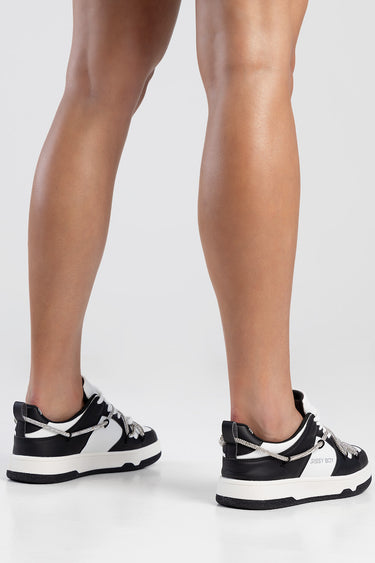 black and white sneakers with silver chain laces on a model’s legs