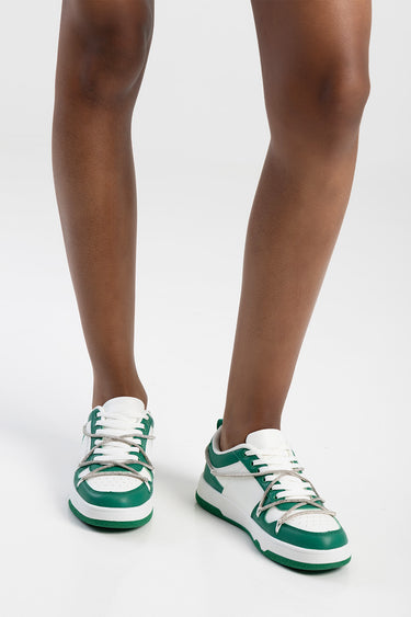 two legs wearing green and white sneakers with white laces on a white studio floor