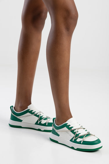 Blue Jean Traders sneakers in green and white with white laces and a green sole on a model's feet