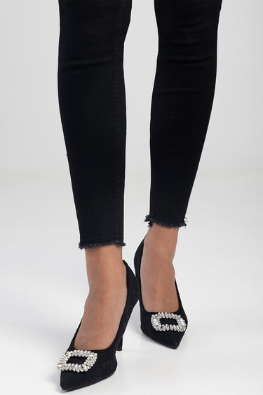 woman wearing black lace court heels with a jeweled square buckle, paired with black frayed-hem jeans