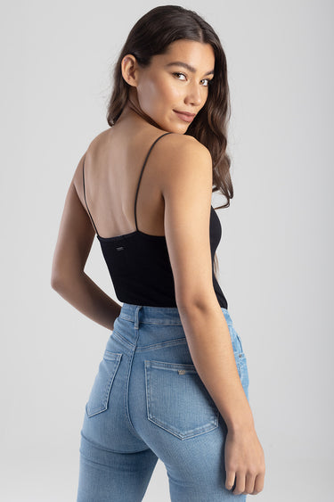 woman in a black spaghetti-strap tank top and light blue jeans, back view with camera on her and slight smile