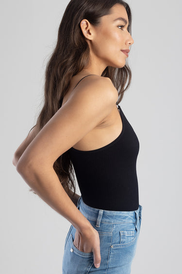 woman wearing a black ribbed tank top with thin straps, in profile, paired with blue jeans
