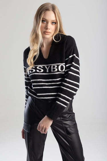 woman wearing a black knit sweater with white stripes and bold letters, paired with black faux leather pants