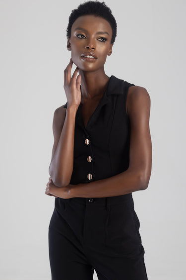 model wearing a black sleeveless waistcoat with gold buttons paired with black trousers in a neutral studio setting