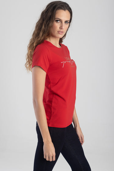 red short sleeve top with a glittery script graphic on the chest, worn by a woman in dark jeans