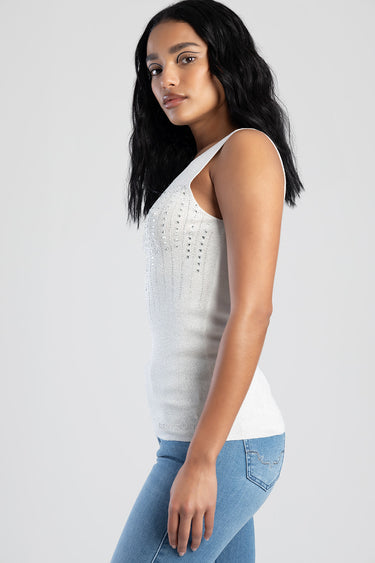 side profile of a woman wearing a white sleeveless tank top with studded embellishments and light blue jeans