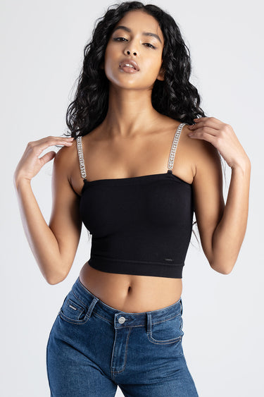 woman wearing black crop top with rhinestone straps and blue jeans, posing against a light background