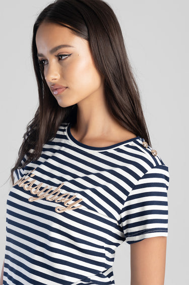 woman wearing navy and white striped short sleeve top with gold shoulder buttons and cursive embroidery across the chest.