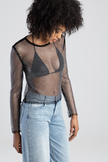 woman wearing a black mesh long sleeve top over a black bra, paired with light wash jeans accented with rhinestones