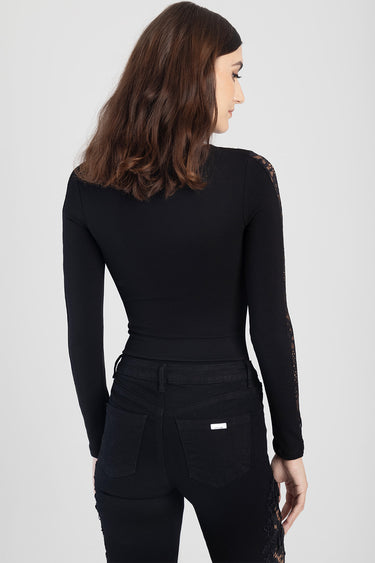 woman wearing black long sleeve bodysuit with lace sleeves, back view, paired with black denim jeans with lace side panels.