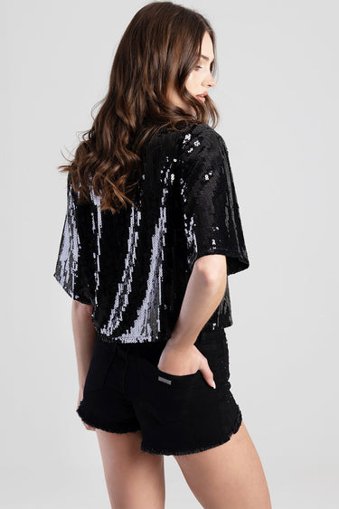 woman in a black sequin short sleeve top with a loose silhouette, paired with black frayed hem shorts, back view