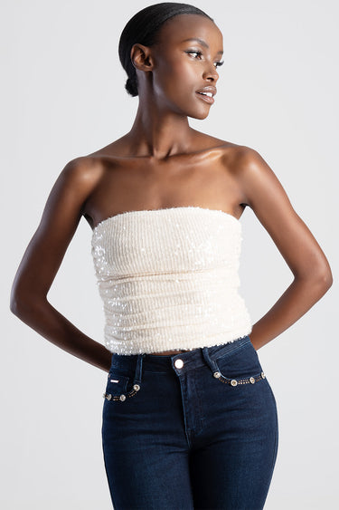 woman wearing a cream strapless sequin top and dark denim jeans with beaded pockets