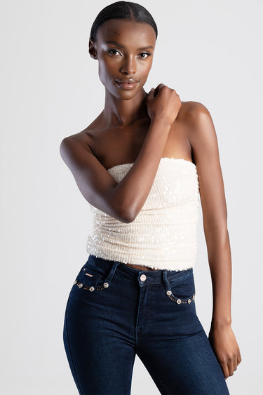model wearing a white strapless sequin top and dark jeans with jewel chain detailing on the pockets