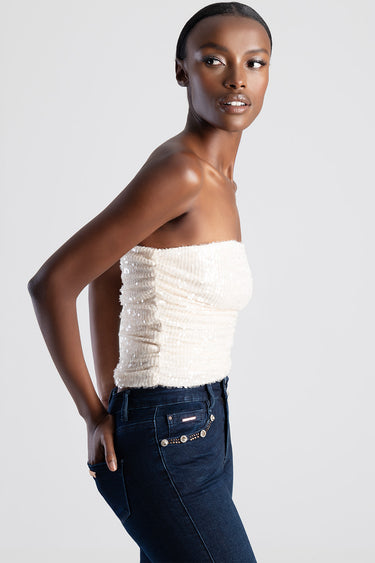 woman in a white textured strapless top and dark jeans with bead embellishments on the pockets, side view