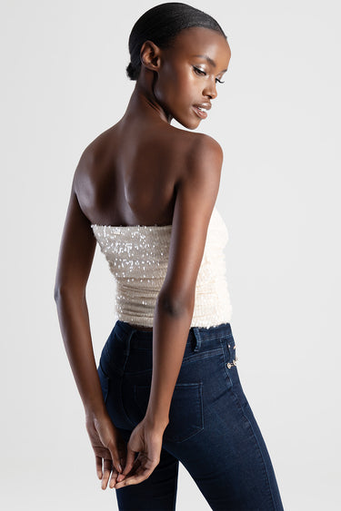 woman in cream sequin strapless top and dark indigo jeans, back view