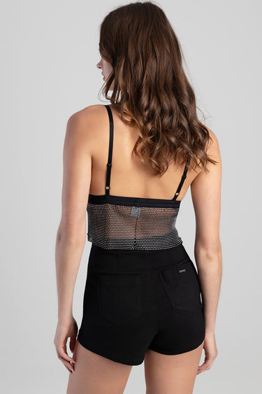 woman wearing a black mesh sequin crop top with adjustable straps and high waist black shorts, back view