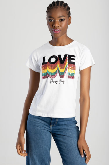 woman wearing a white short sleeve top with a rainbow sequin love graphic and small script beneath, paired with blue jeans