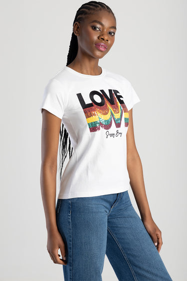 woman wearing white short sleeve top with rainbow sequined love graphic and blue jeans