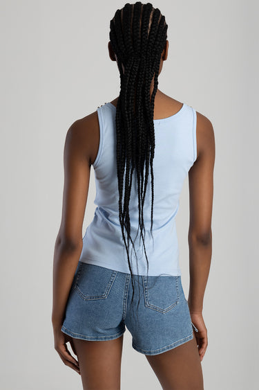 back view of a model wearing a light blue knit sleeveless vest and denim shorts with long braids