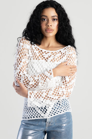 woman wearing a white crochet net top with circular sequins, long sleeves, over a white inner layer, paired with metallic