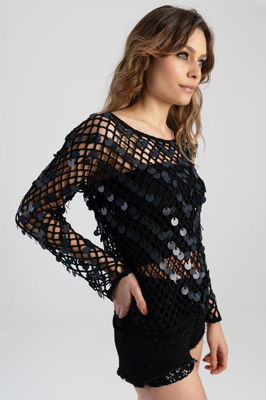 woman in a black mesh top with round sequins and long sleeves, shown in side profile