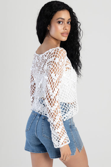 woman wearing a white crochet knit top with circular motifs over a white tank, paired with denim shorts