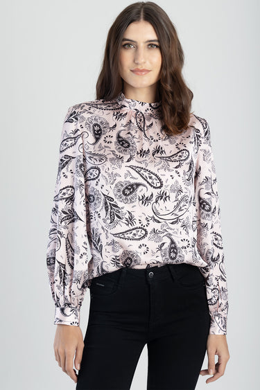 woman wearing a pale pink paisley long sleeve blouse with a high neck, tucked into black jeans