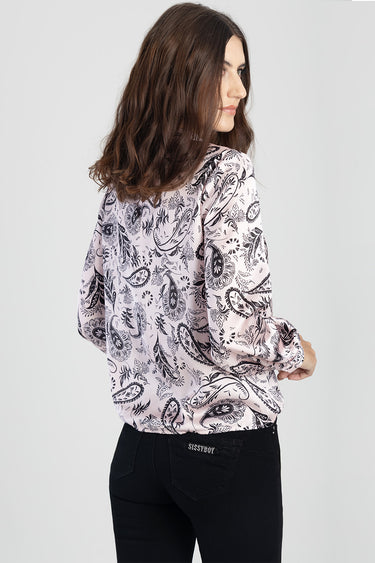 back view of a woman wearing a light pink paisley print blouse with long sleeves over black jeans