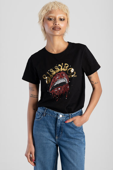woman wearing a black short sleeve top with red sequined lips and gold lettering, paired with blue jeans