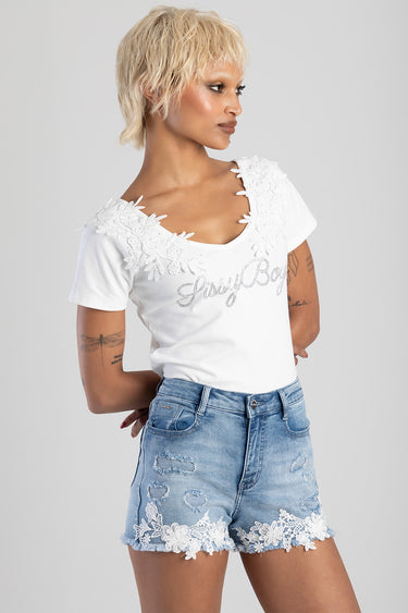 model wearing a white top with lace floral neckline and hem trim, paired with light wash denim shorts with lace edging