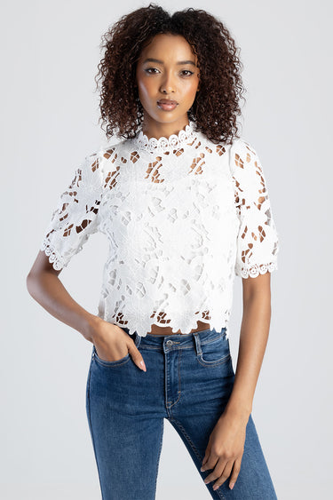 woman wearing white lace top with floral pattern, high neckline and short sleeves, cropped hem, paired with blue jeans