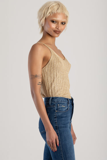side view of a woman in a gold knit vest top and blue denim jeans