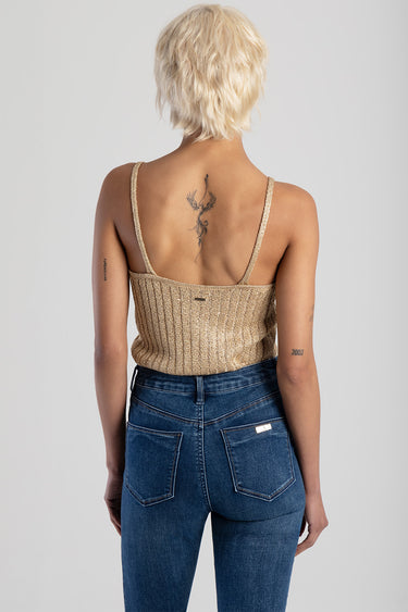 woman seen from behind wearing a gold knit vest with thin straps and blue jeans; visible spine tattoo
