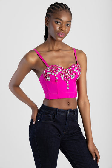 woman wearing bright pink cropped corset top with rhinestone embellishments and thin straps, paired with dark denim jeans