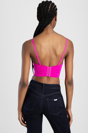 back view of a bright pink corset top with adjustable straps and back closure, paired with dark denim jeans