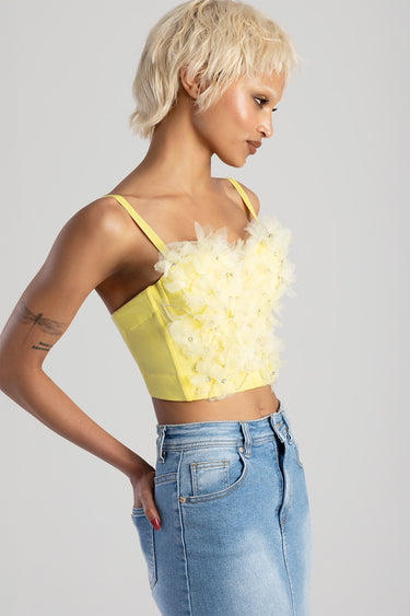 side profile of a woman wearing a yellow crop top with tulle flower embellishments and thin straps, paired with light blue