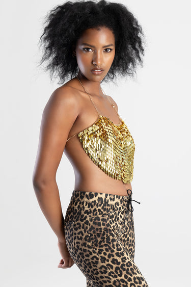 woman wearing a gold sequin halter top and leopard print pants posing against a light background
