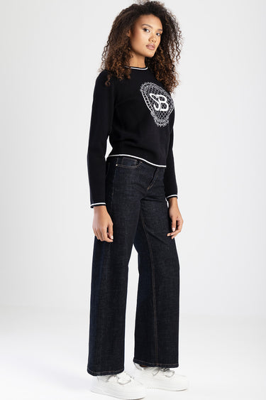 woman in navy knit sweater with a light logo on the chest, white piping at the hem and cuffs, paired with dark wide-leg