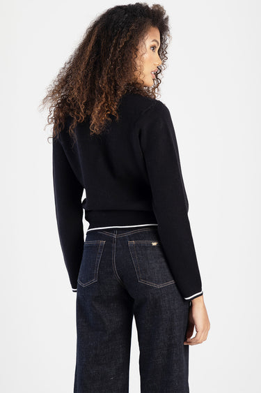 woman wearing a navy knit sweater with white trim at the hem and cuffs, with dark denim jeans, shown from the back