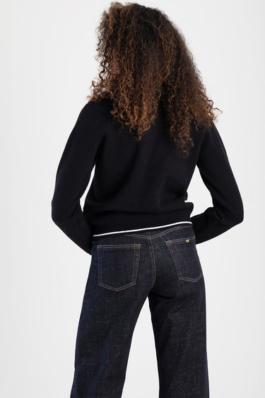 woman in a navy knit sweater with a white striped hem, paired with dark denim jeans, back view