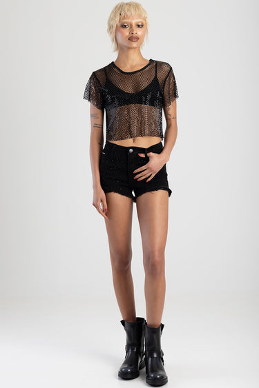 model wearing a sheer black mesh cropped top over a black bra, distressed black denim shorts, and black combat boots