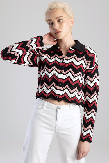model wearing a cropped zigzag knit sweater in black white pink and red with a dark collar, paired with white jeans