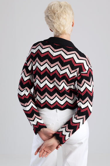 woman with short blond hair wearing a black, white and pink chevron knit sweater seen from behind