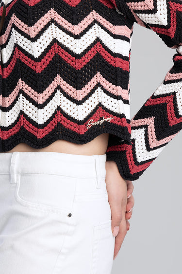 cropped knit sweater with pink white black and red chevron pattern and logo at hem, paired with white denim jeans