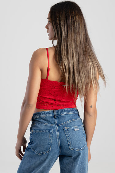 woman in red lace crop top with thin straps and blue jeans, back view