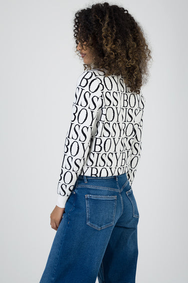 woman from behind wearing a white knit sweater with a bold black letter pattern and blue jeans.