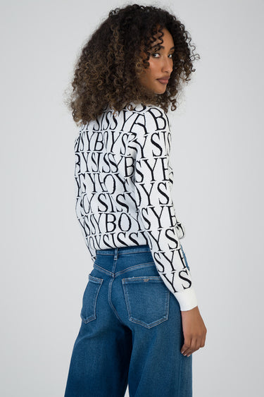 woman wearing a white knit sweater with black bold letters and blue jeans, side view