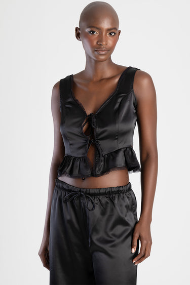 model wearing a black satin crop top with lace trim, front ties and a ruffled hem