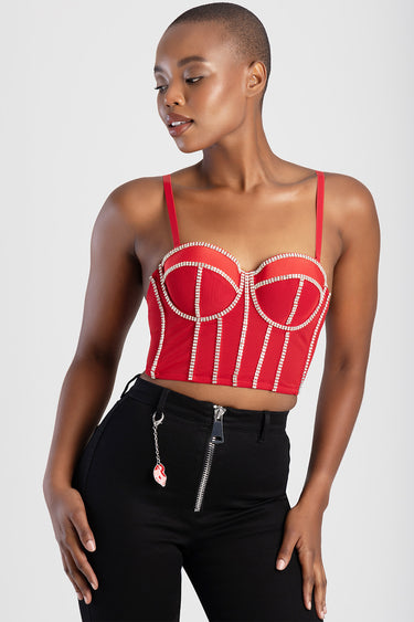 woman wearing a red embellished corset top with rhinestone trim and thin straps, paired with black high waisted pants with