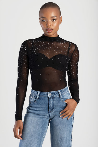 model wearing black sheer top with small rhinestones over a black bralette with blue jeans
